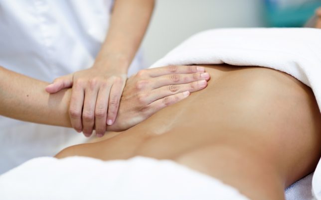 Hands massaging female abdomen.Therapist applying pressure on belly. Woman receiving massage at spa salon